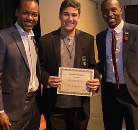 Three men pose for picture middle man holds diploma
