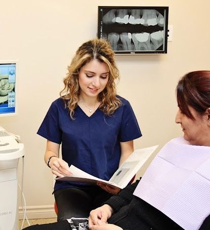 A woman in a blue scrub is talking to another woman in a dental chair