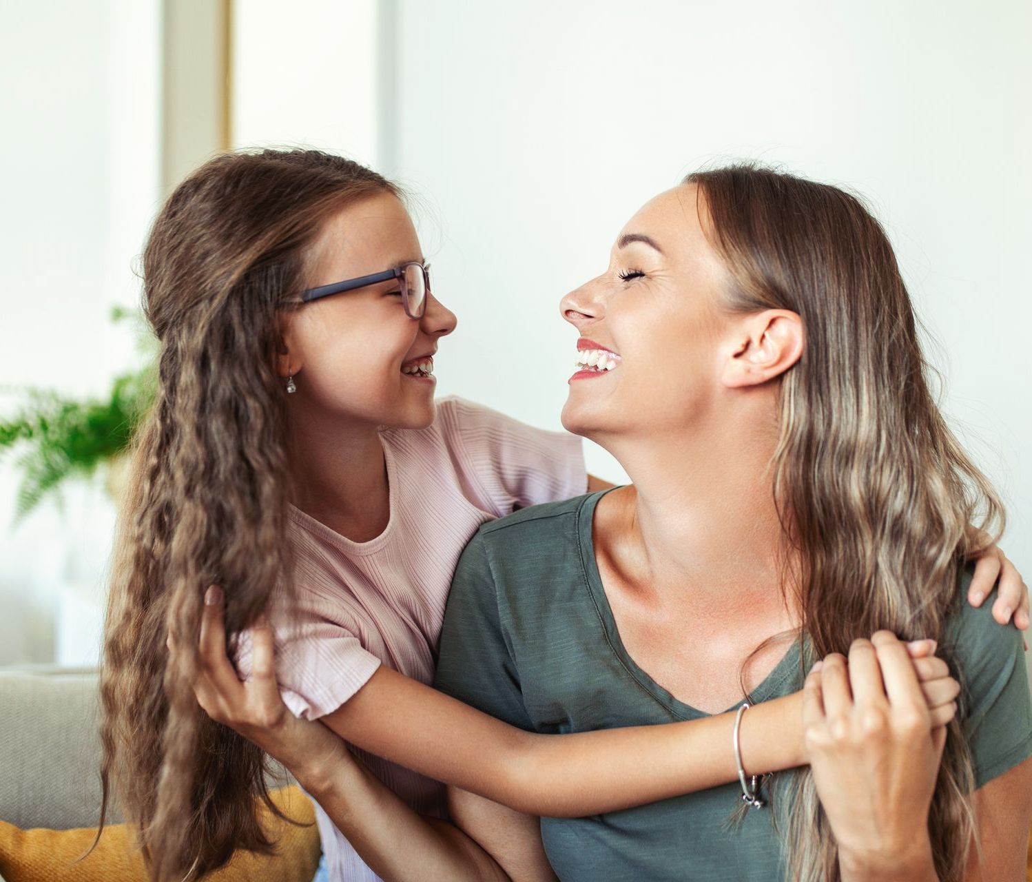 A woman and a little girl are sitting on a couch and hugging each other.