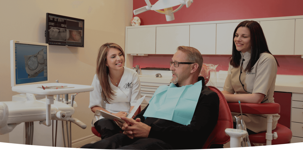 Un homme est assis sur une chaise dentaire et parle à deux femmes.