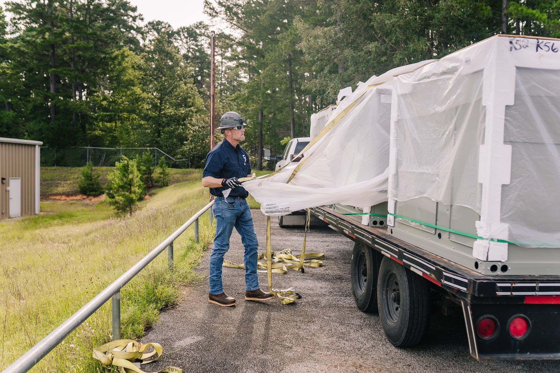 Man securing tarp on cargo on a flatbed truck outdoors, wearing jeans, a hat, and gloves.