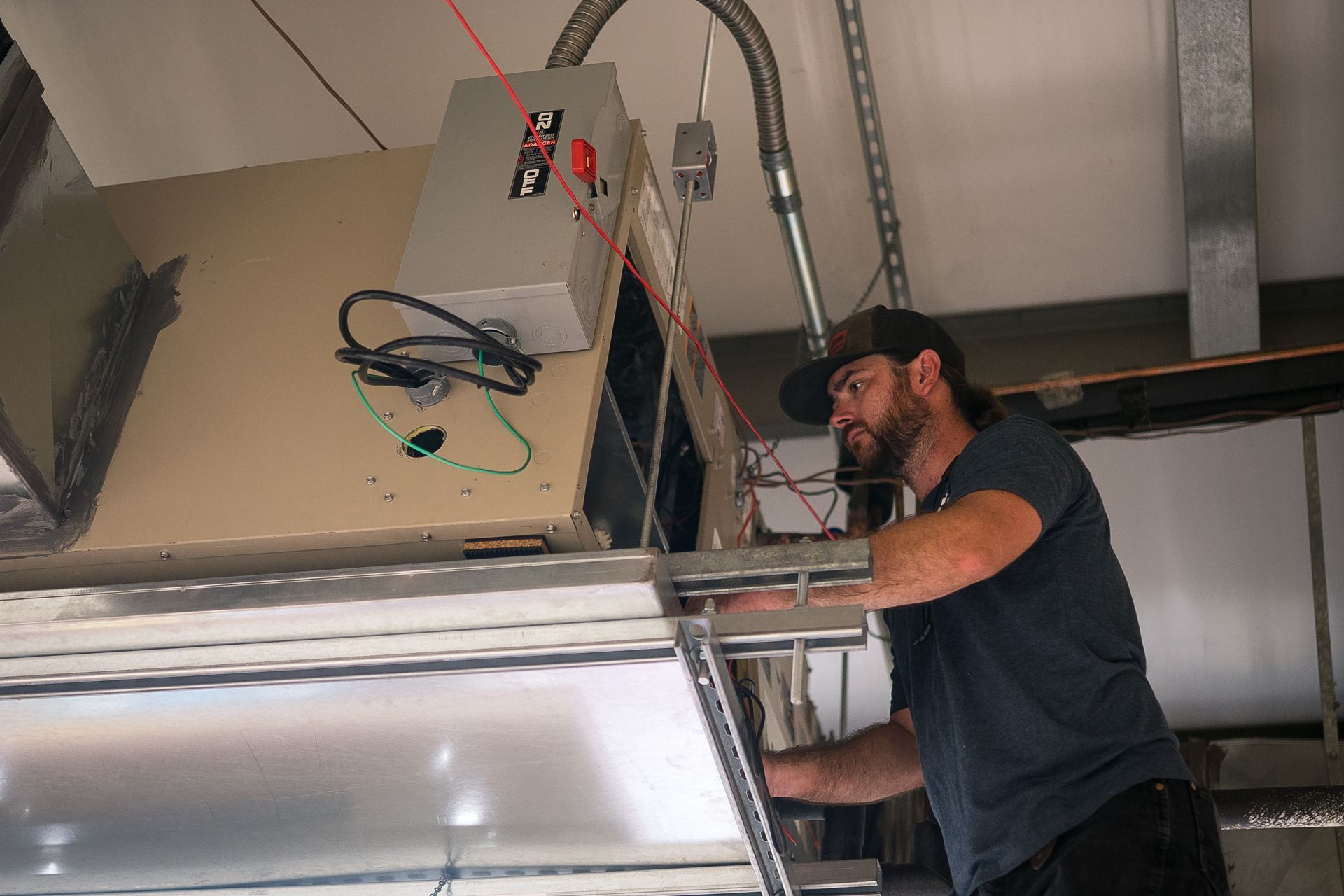 Man working on HVAC system, gray box, metal ductwork, indoor, focused.