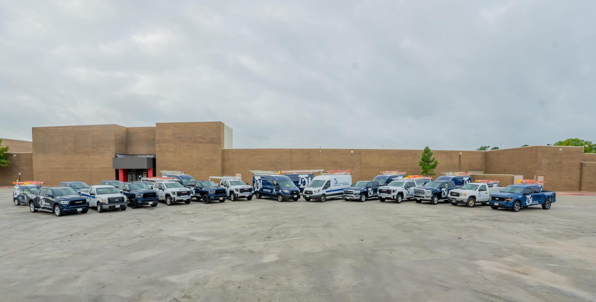 A large group of service vans parked in front of a brick building under a cloudy sky.