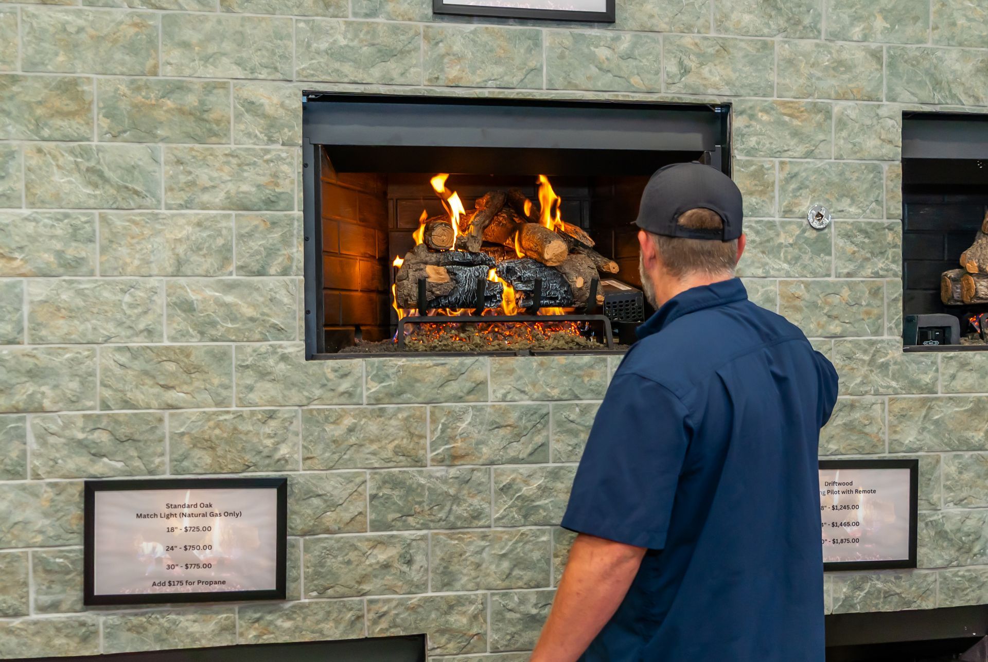 Man in blue shirt looks at fire burning in a fireplace in a brick wall setting.