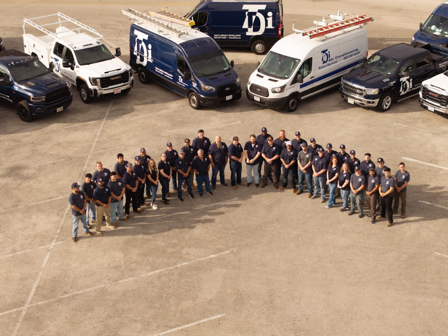 Group of employees in blue shirts standing in front of company vehicles with the company logo.