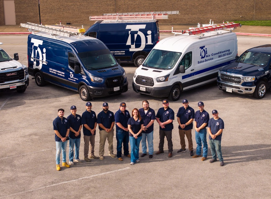 Team of HVAC technicians with service vehicles, wearing blue shirts and hats, standing outdoors.