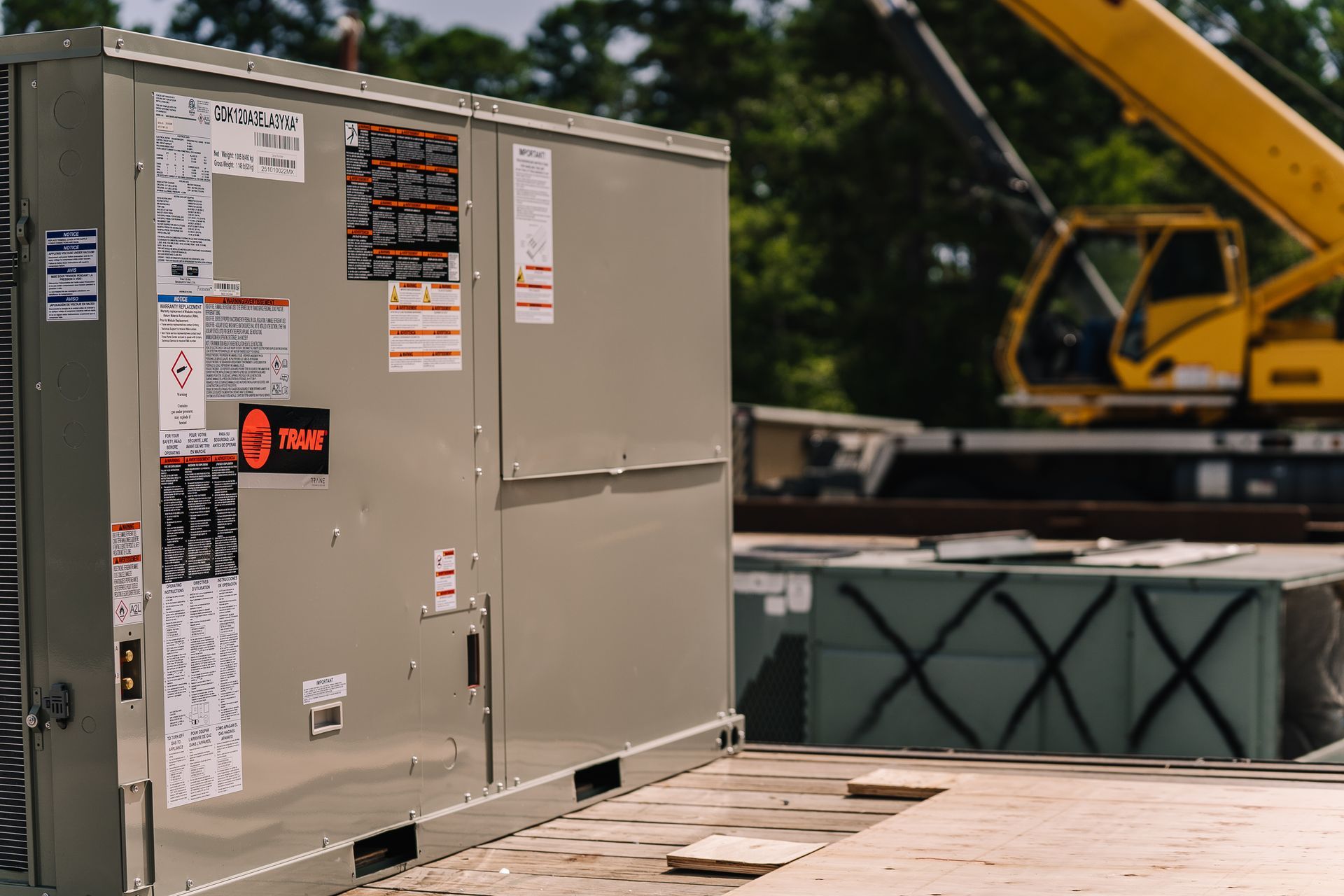 Large, beige HVAC unit on a construction site, with a yellow crane and wood planks in the background.