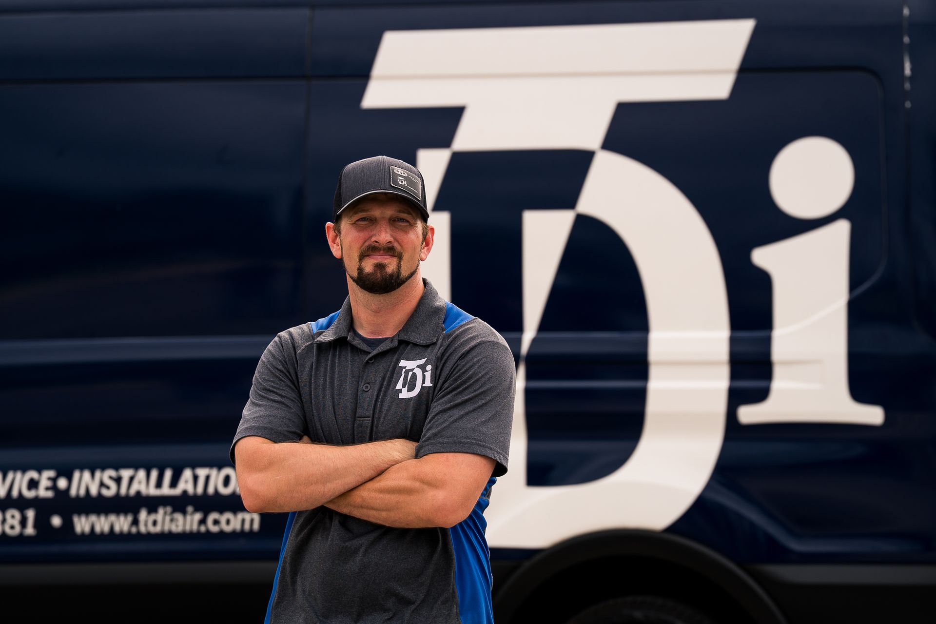 Man with arms crossed in front of a dark blue van with white 