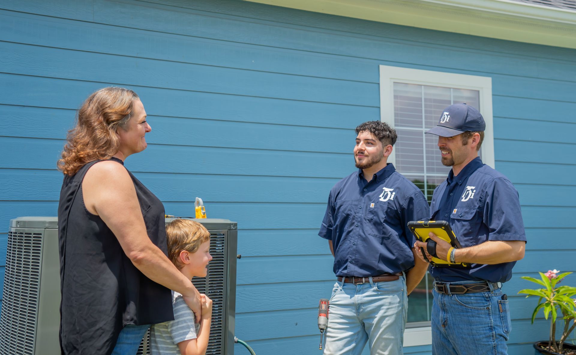 Woman and child talk with two technicians near a blue house and AC unit.