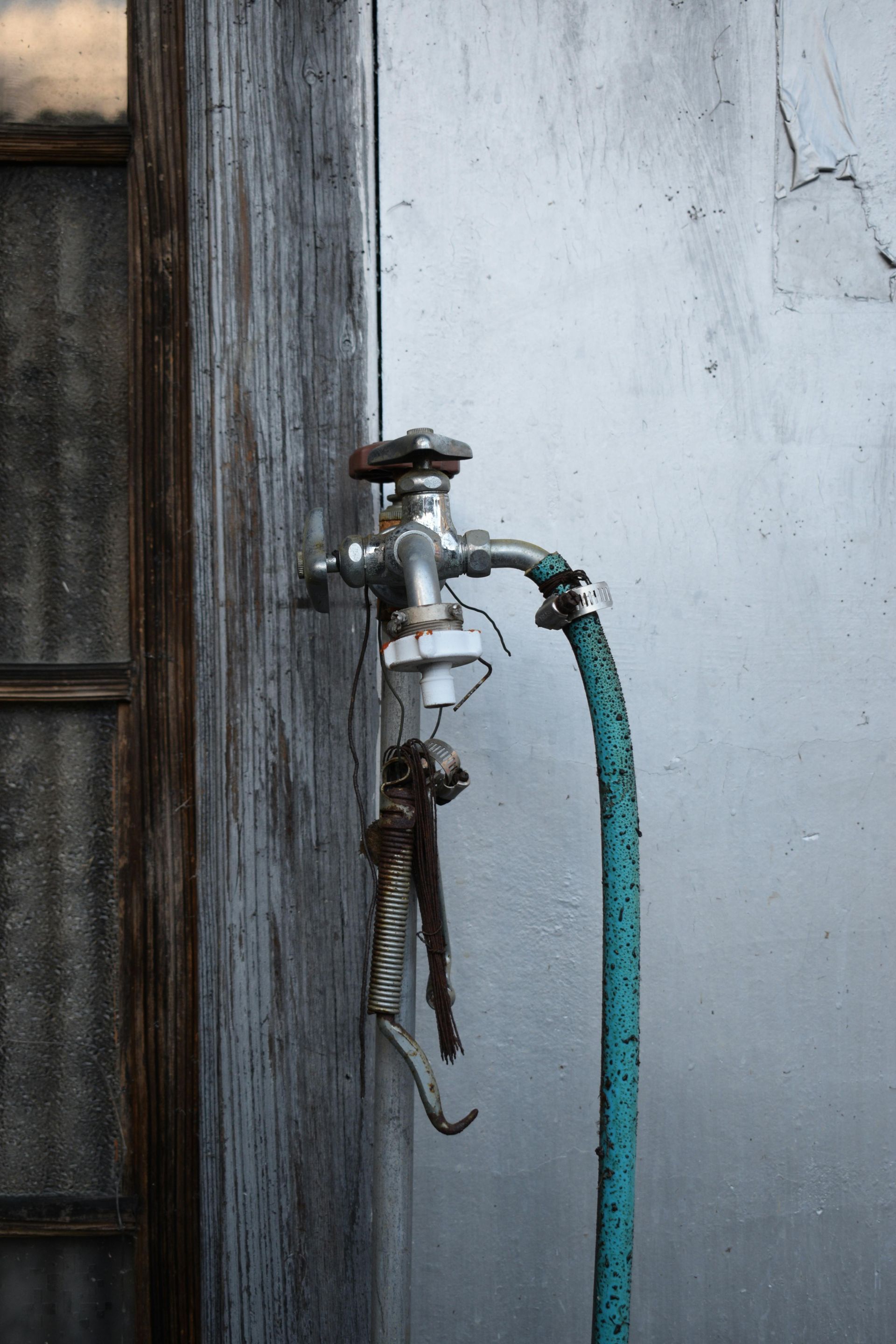 Faucet with attached hose and pliers hanging on a weathered wall next to a window.