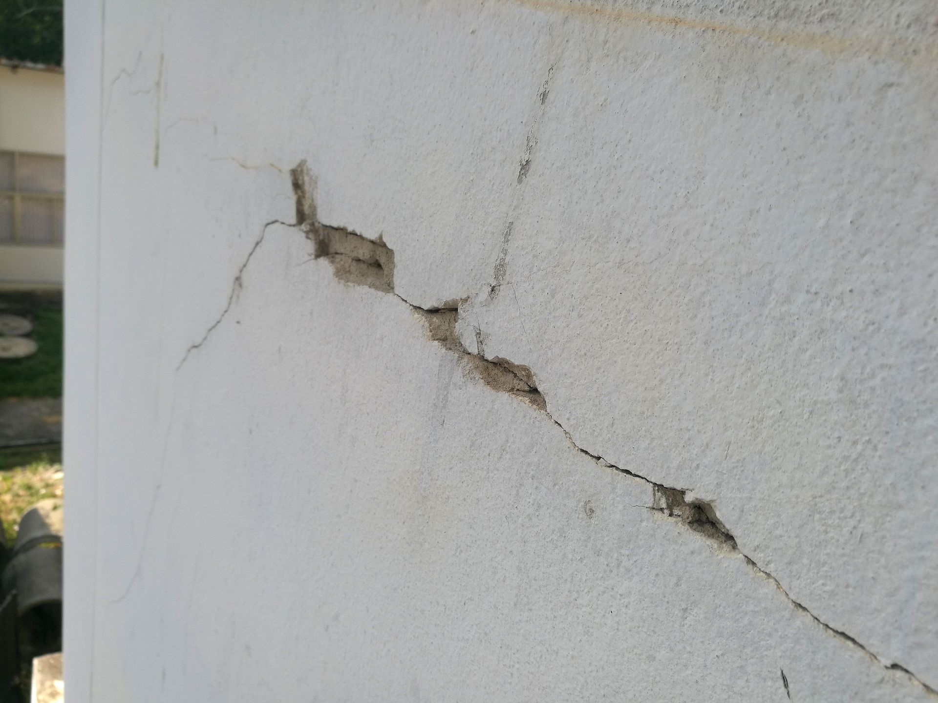 Cracked white stucco wall, showing damage and exposed interior material.