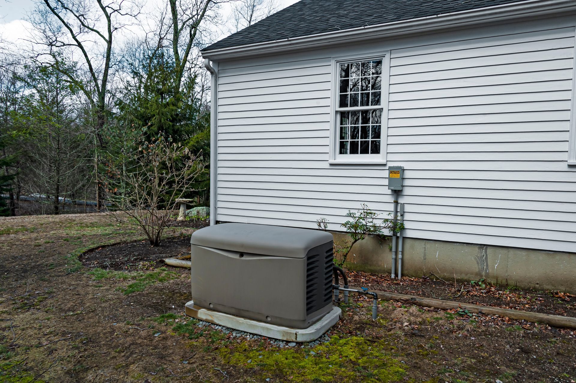 Tan generator on a concrete pad next to a white deck on a grassy lawn.