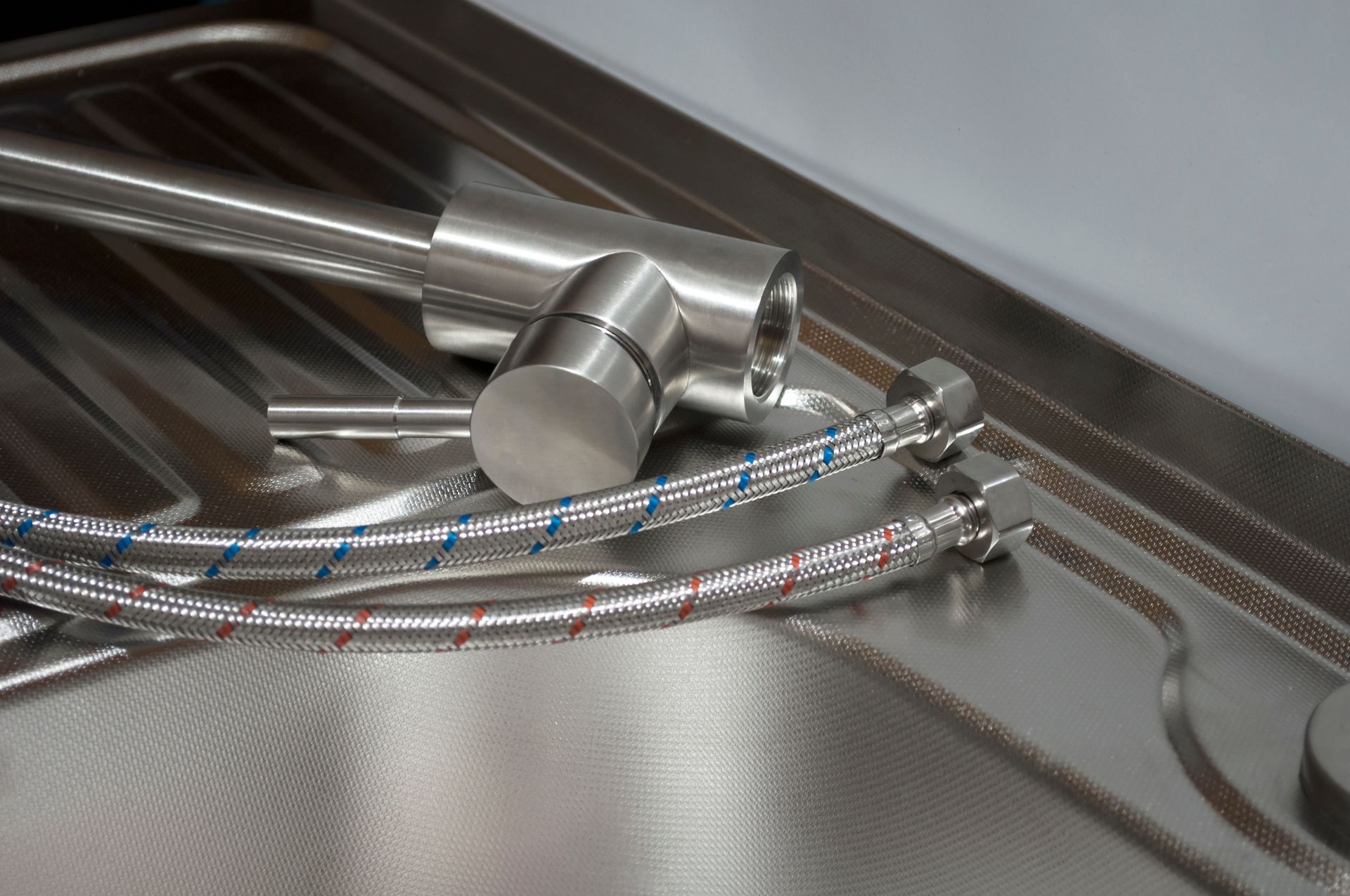 Stainless steel faucet and water lines inside a sink basin.