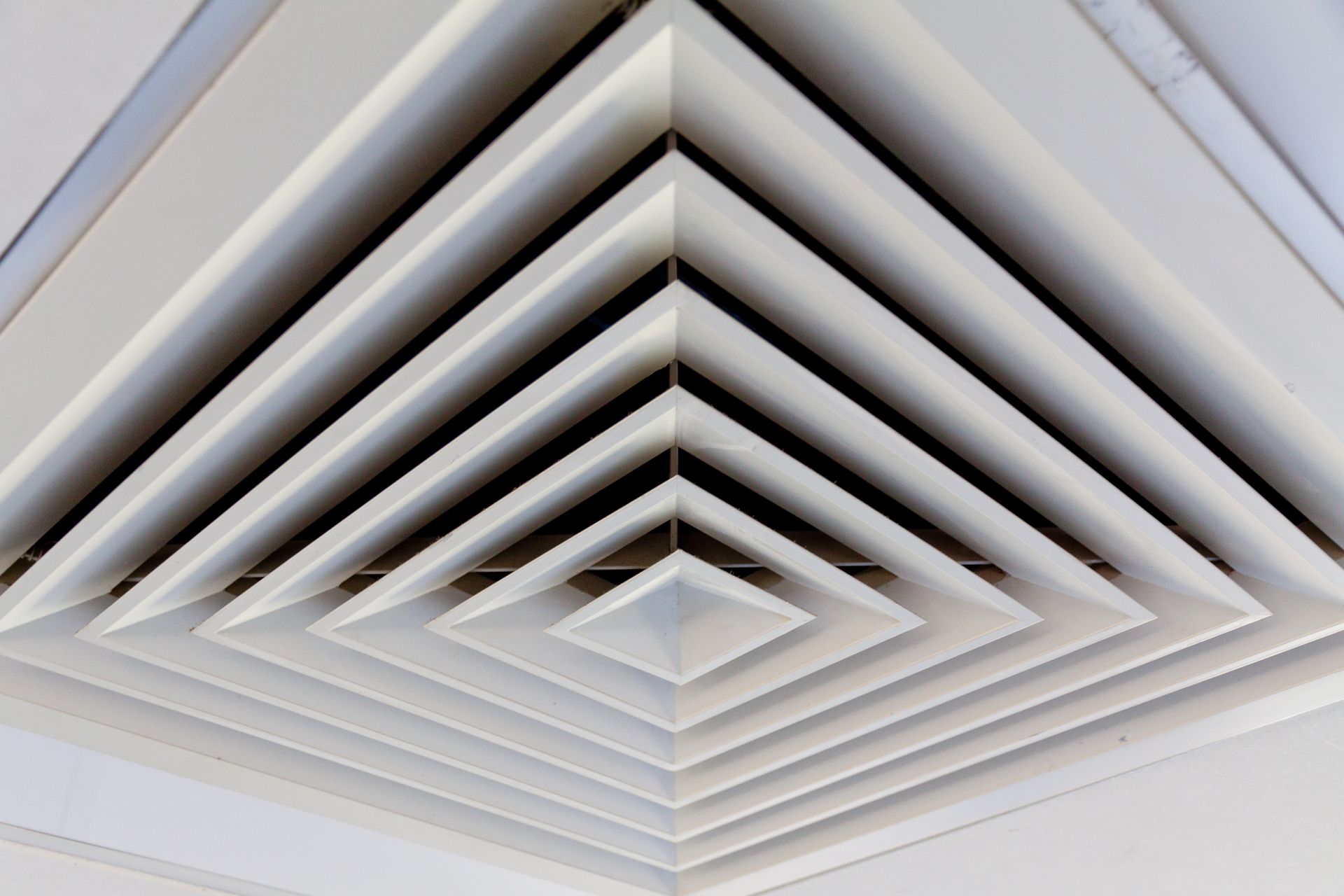 White, square air vent with geometric, layered design on a ceiling.