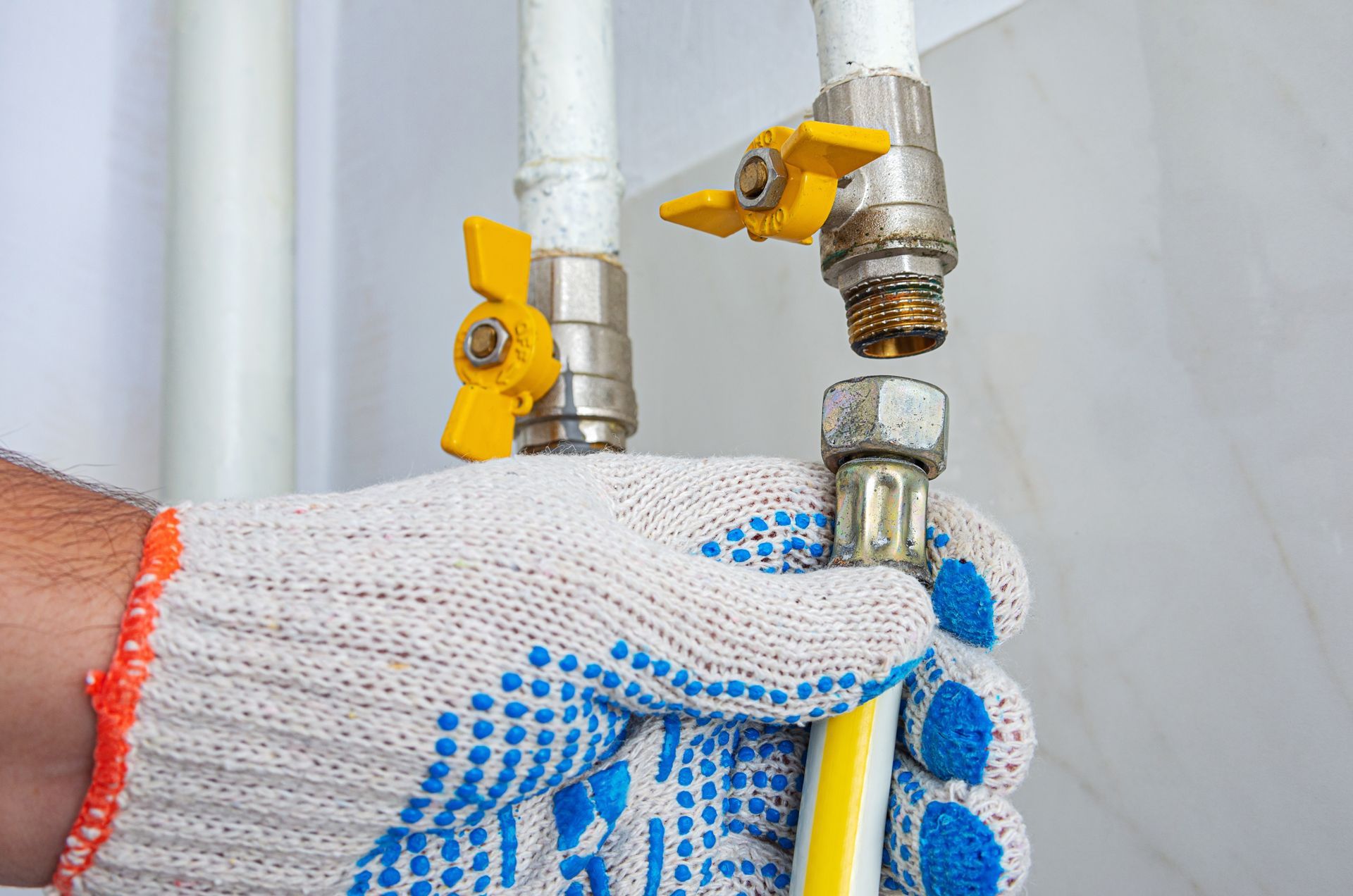Hand in glove connecting a yellow gas hose to a pipe with yellow valve.