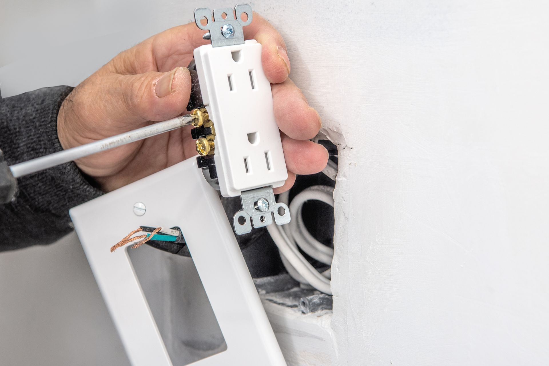Person installing a white electrical outlet in a wall, using a screwdriver.