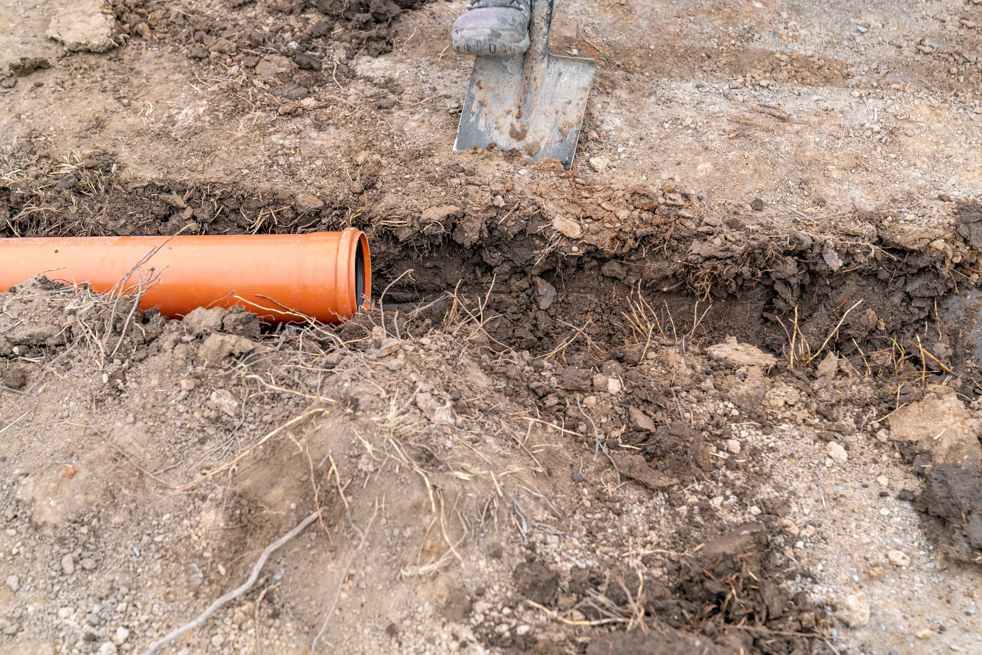 Orange pipe in a dirt trench with a shovel, ready for burial.
