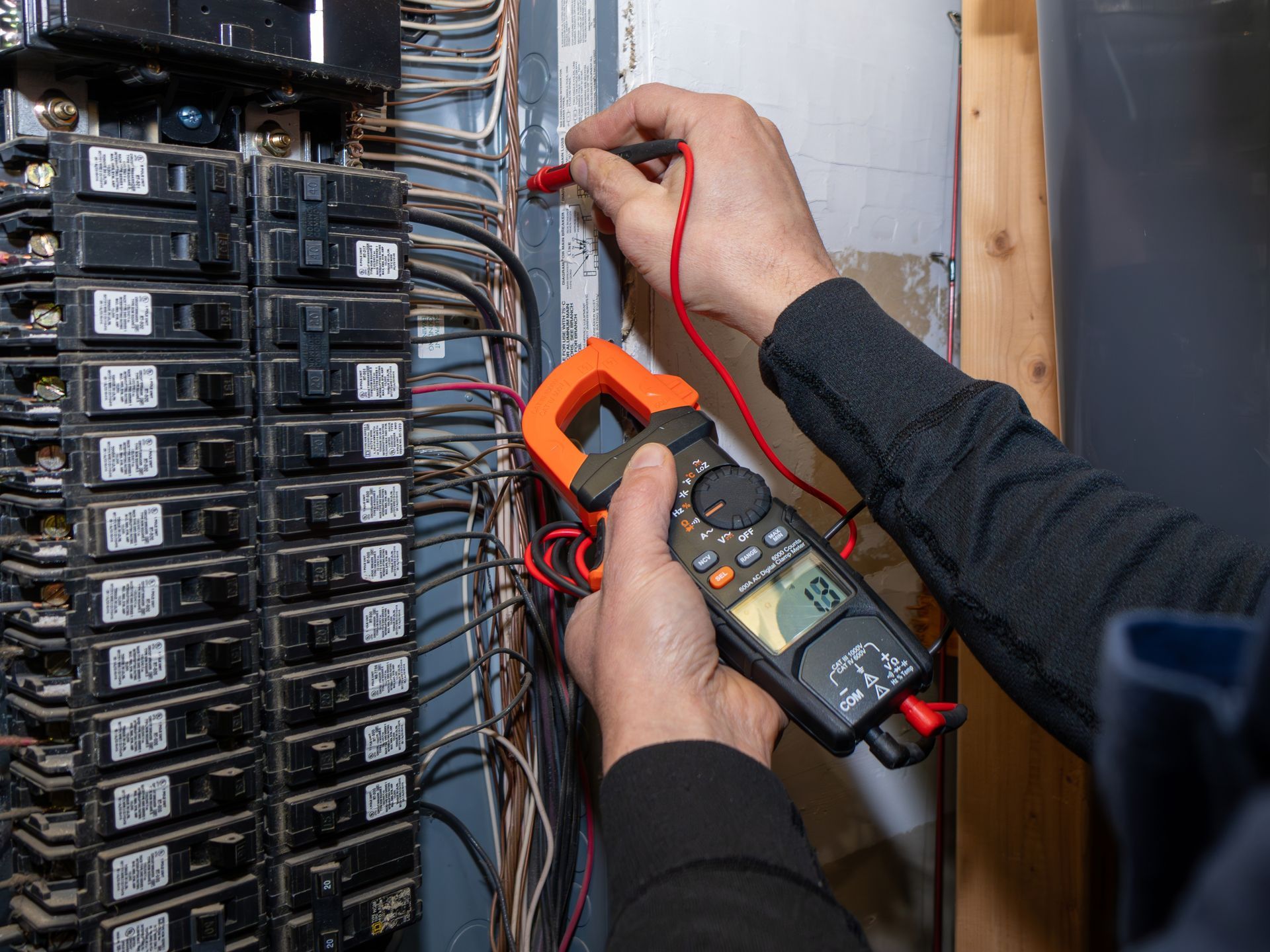 Electrician testing wires in a breaker panel with a multimeter.