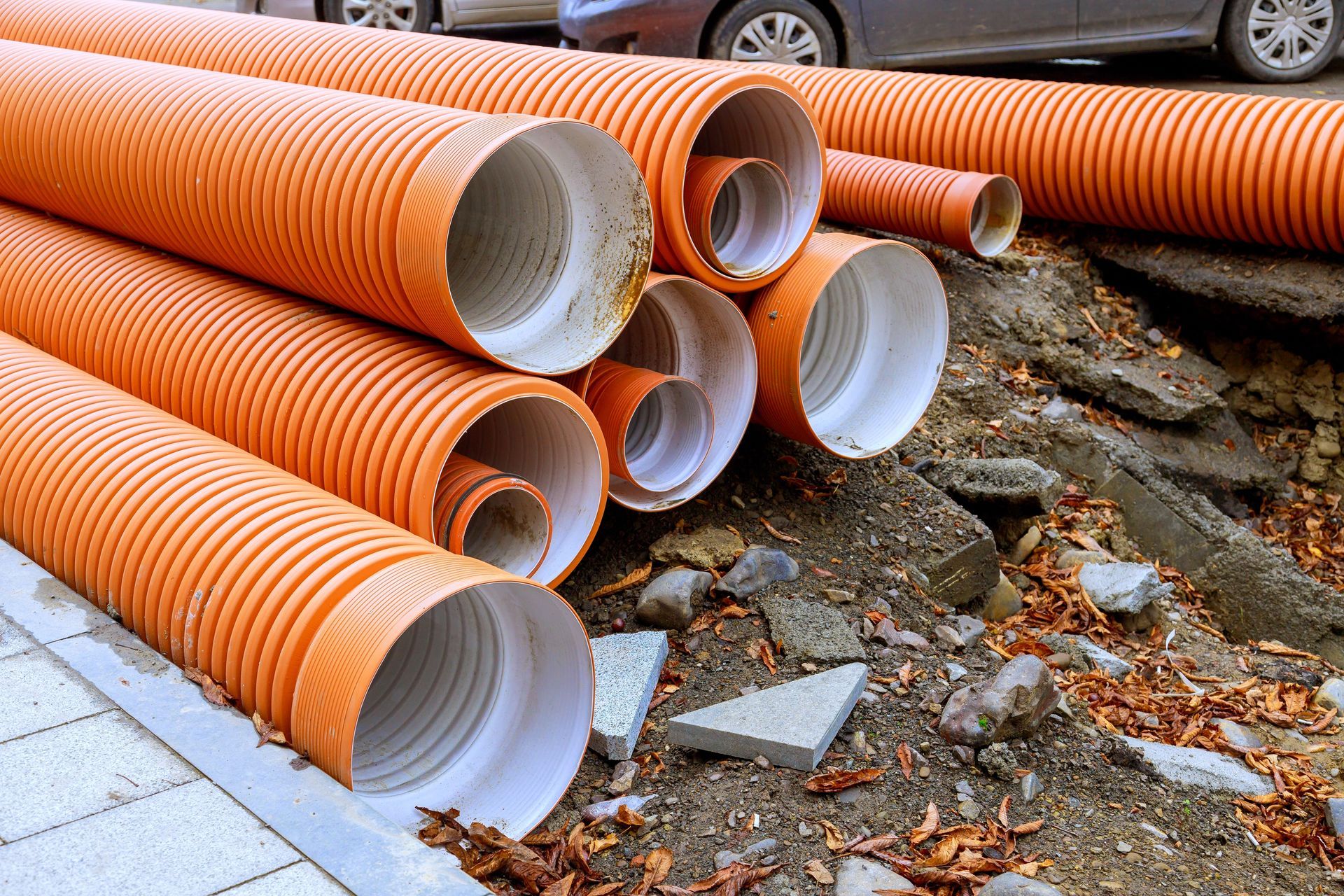 Person installing orange plastic plumbing fitting in a trench, working outside.