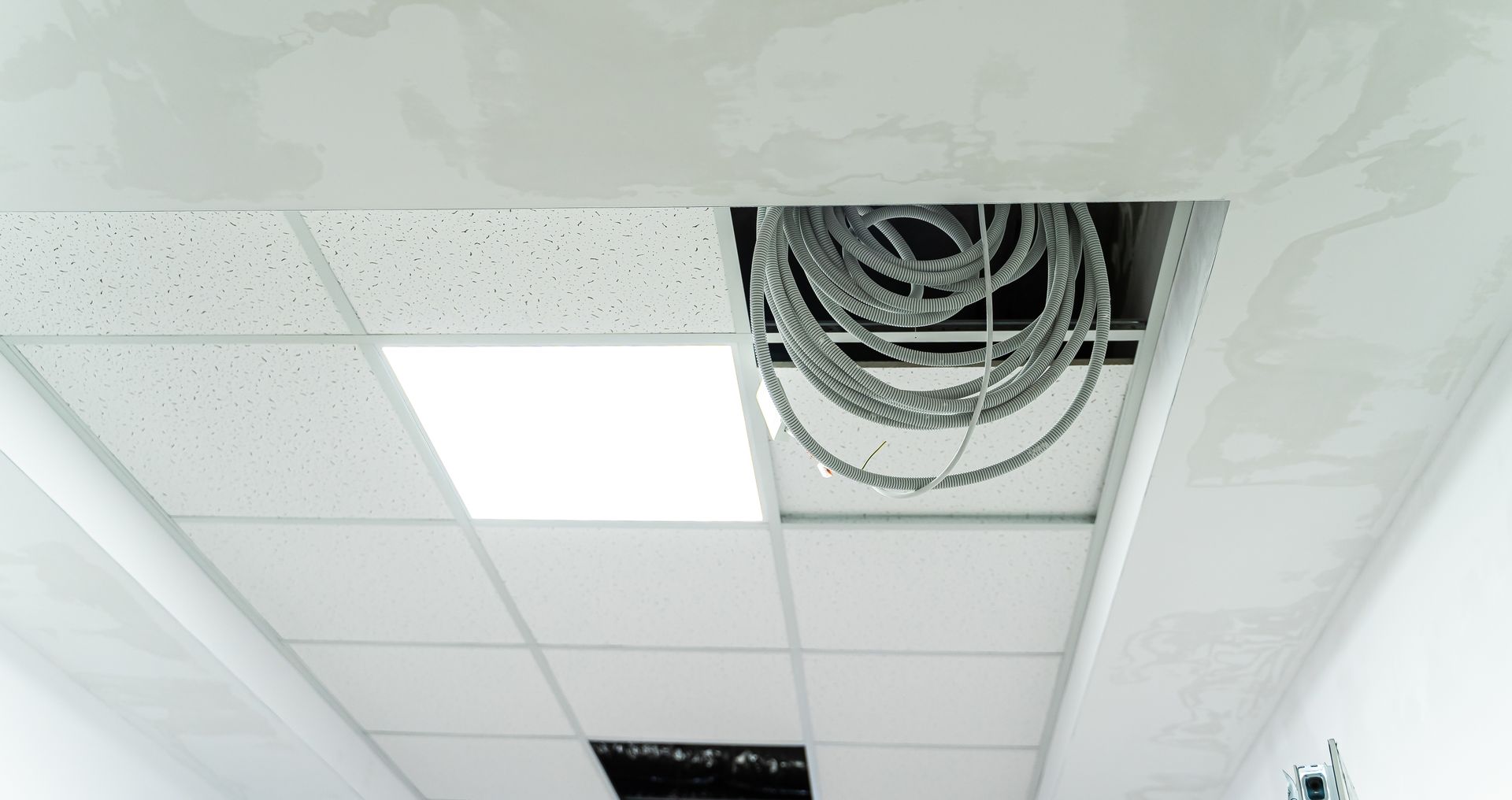 A view of an open ceiling panel revealing electrical wires in a white, finished ceiling.