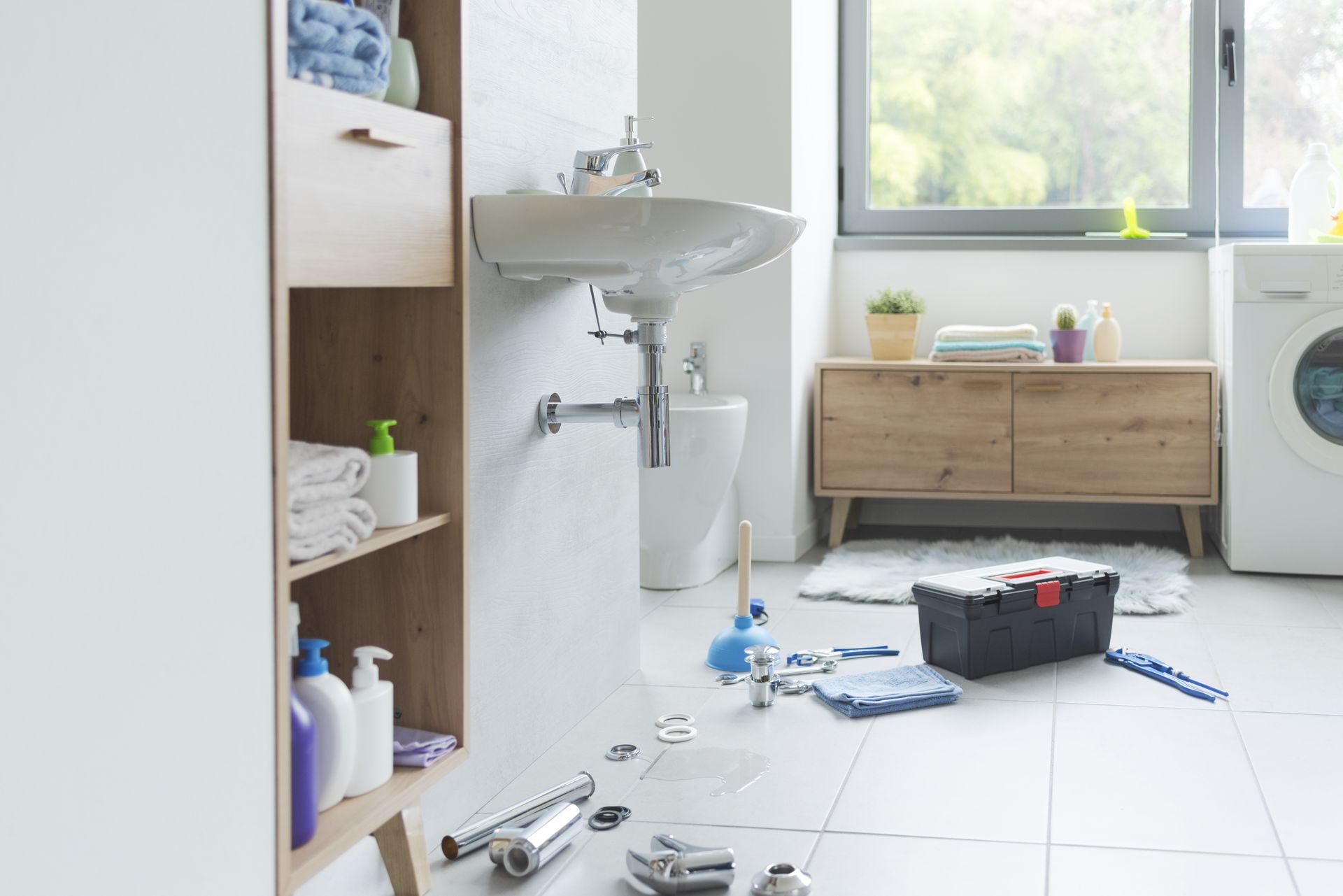 Bathroom scene with plumbing tools, a leaky sink, and a toolbox on the floor.