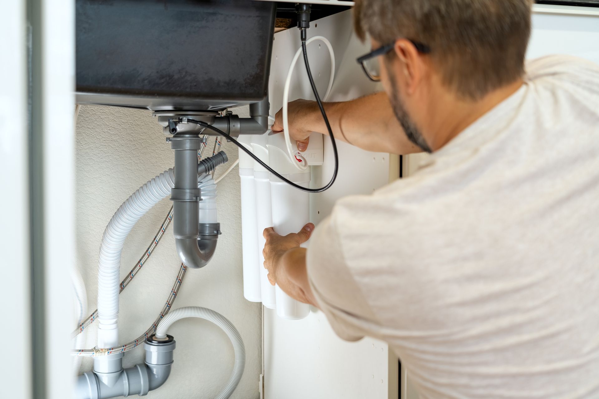 Man installs a water filter under a kitchen sink.