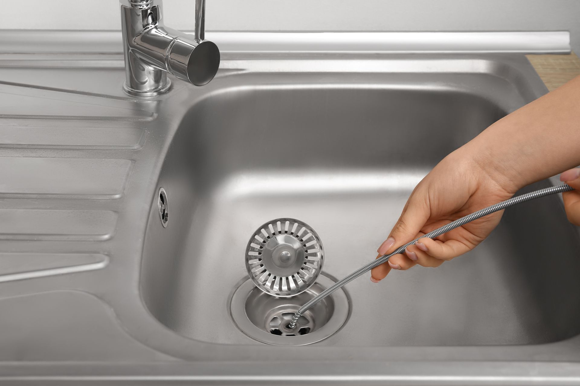 Person cleaning a stainless steel kitchen sink drain with a strainer tool.