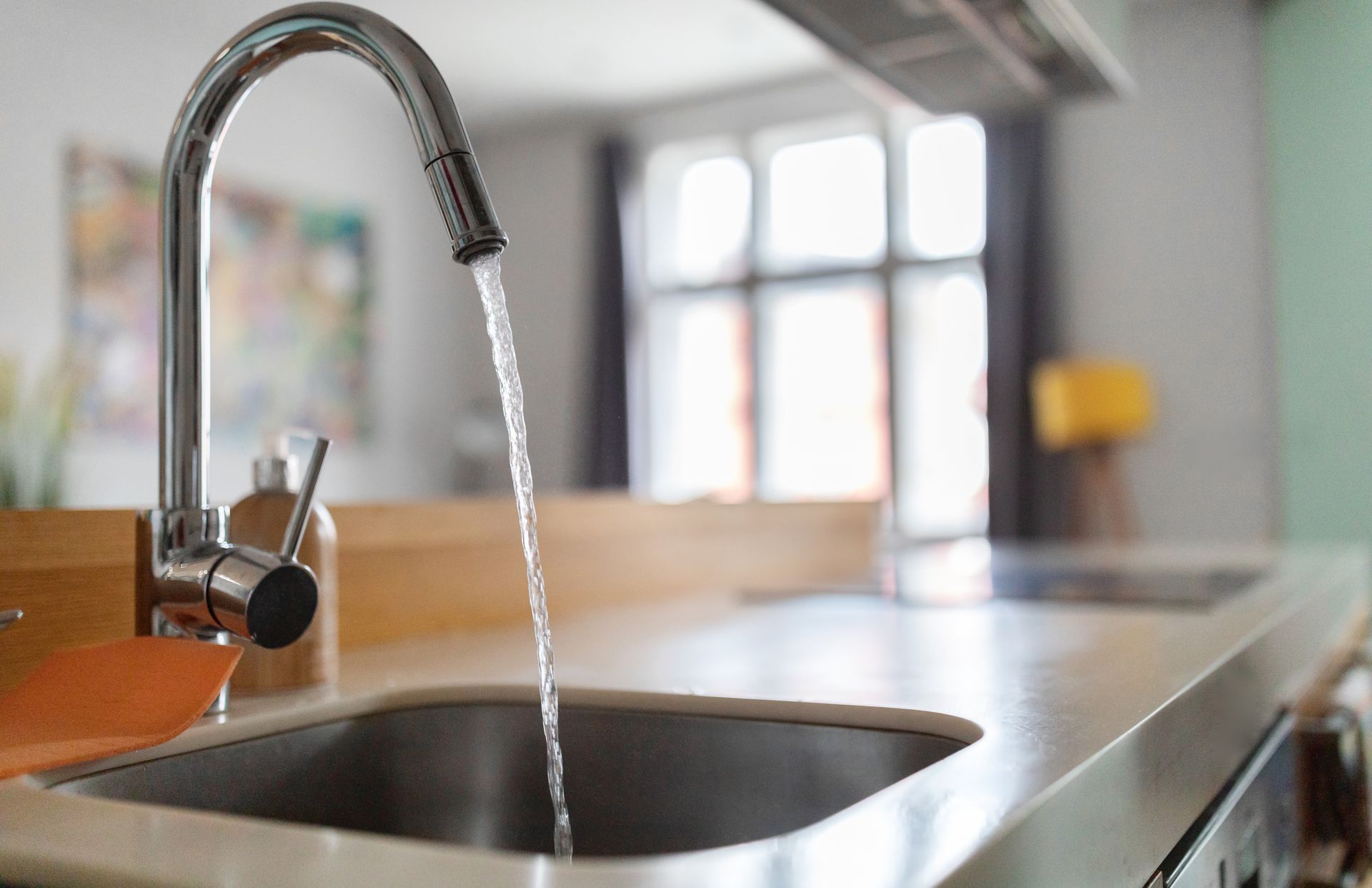 Faucet with water flowing into a stainless steel sink, countertop in a kitchen.
