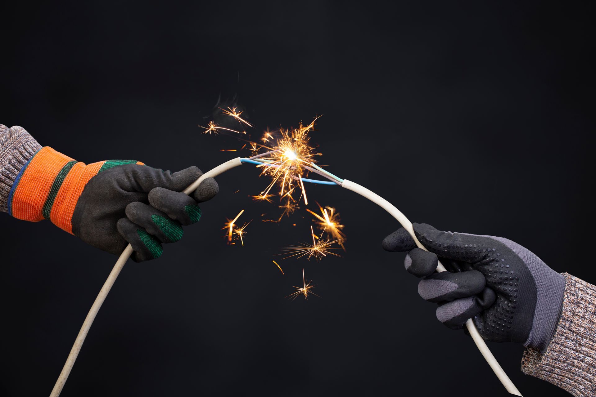 Hands in gloves holding sparking electrical wires.