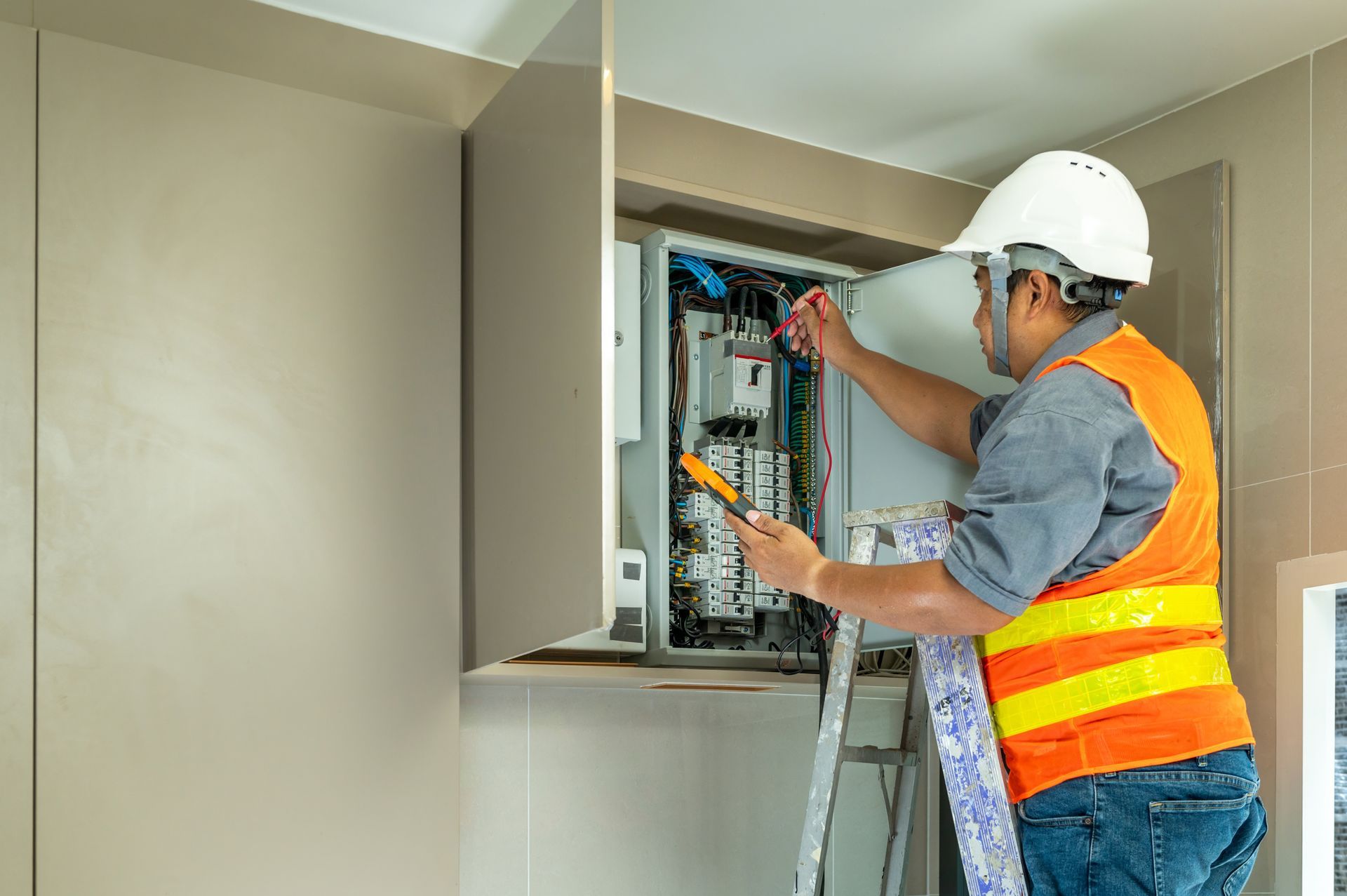 Electrician in a hard hat and safety vest working on electrical panel.