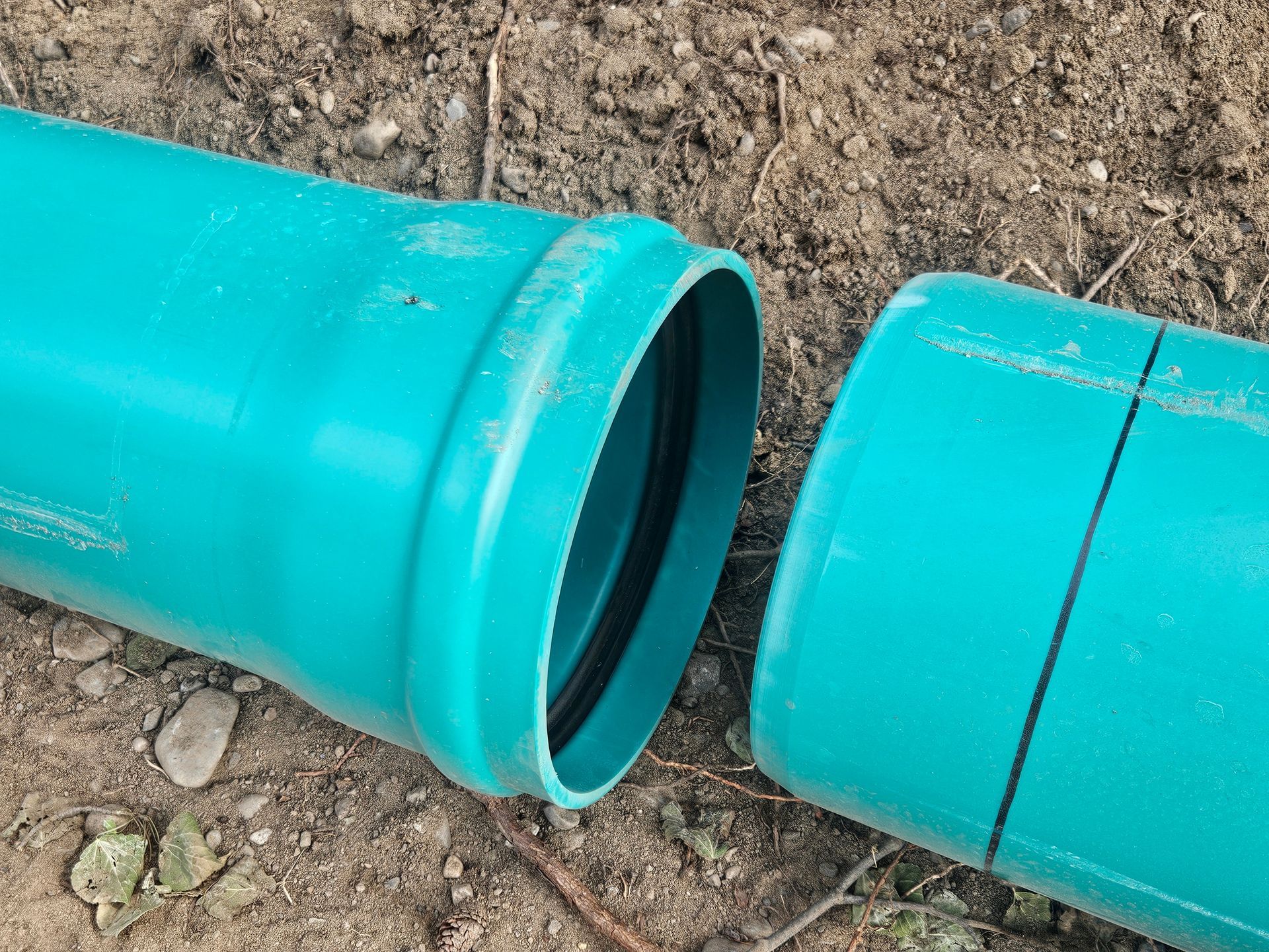 Open corrugated pipe next to a wall, with black tubing and a yellow rope leading into it; the lid is nearby.