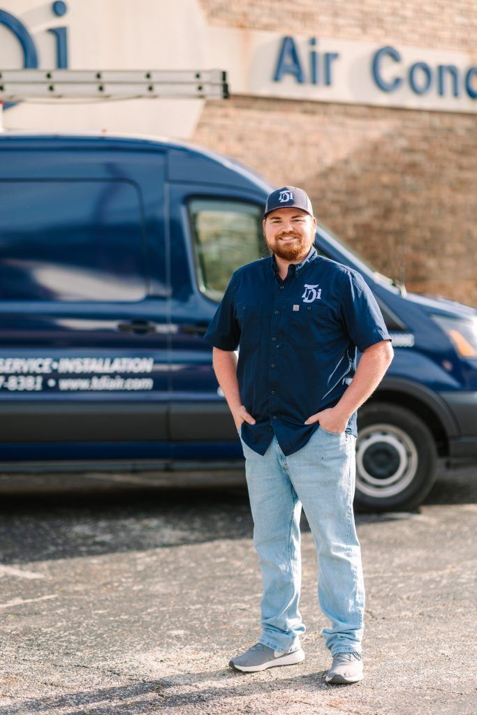 Man in blue shirt and jeans stands by a dark blue service van; 
