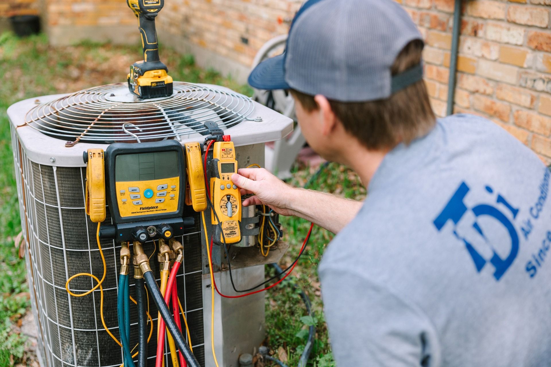 HVAC technician in gray shirt checking air conditioner unit with diagnostic tools outside.