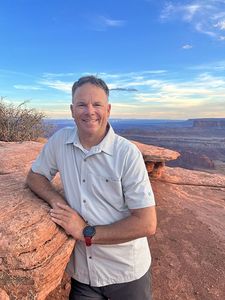Jason Taylor smiling with his elbow resting on a sandstone boulder.
