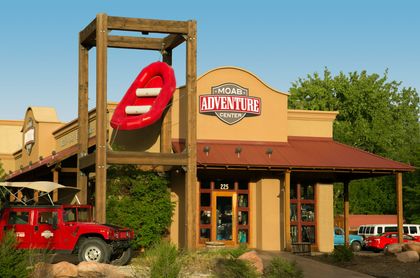 The front of the Moab Adventure Center building with a red raft hanging in a tower and a red hummer parked to the side.