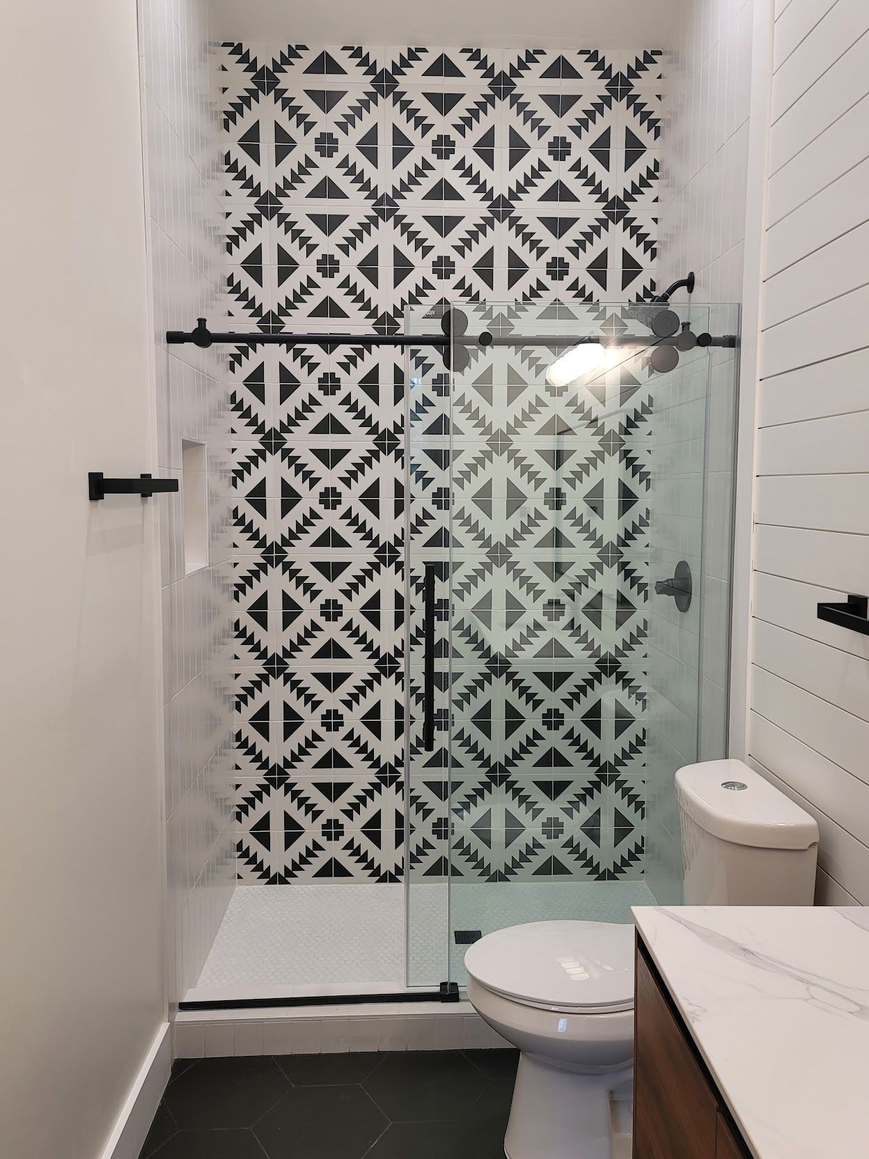 A bathroom with a toilet and a shower with a black and white tile wall.