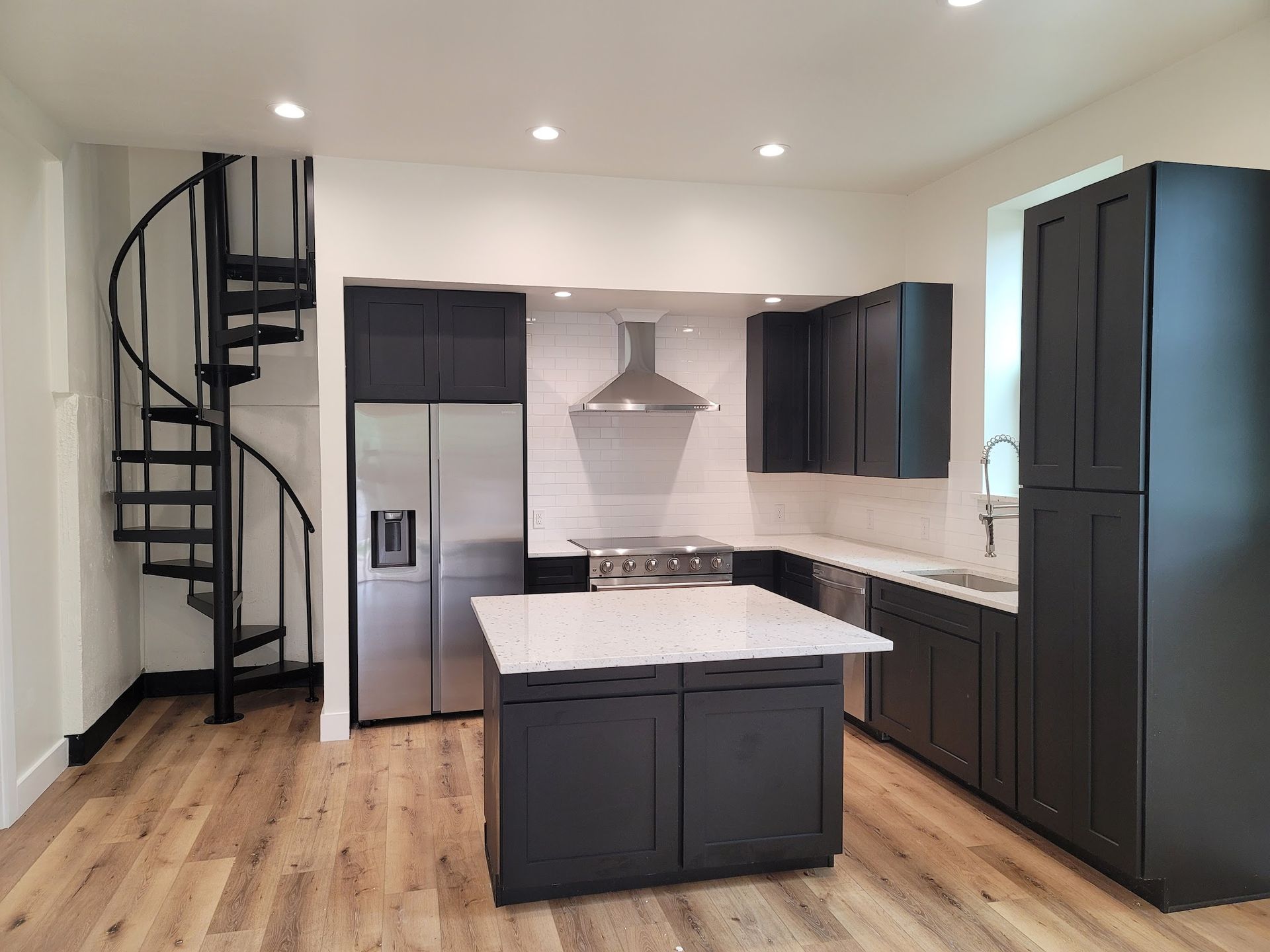 A remodeled kitchen with black cabinets and a spiral staircase