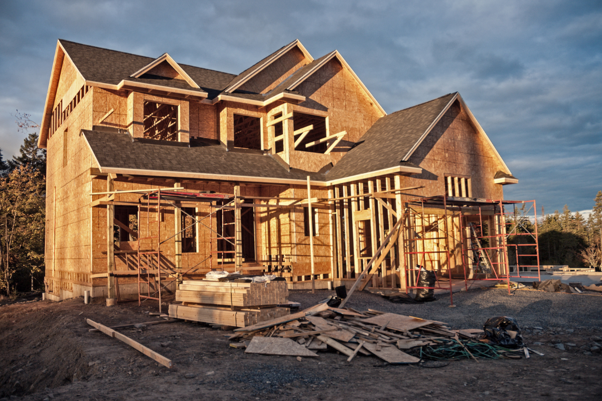 A large house is being built in the middle of a dirt field.