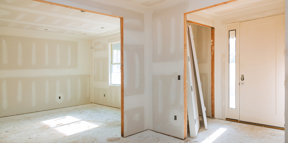 An empty room with drywall walls and a door in a house under construction.