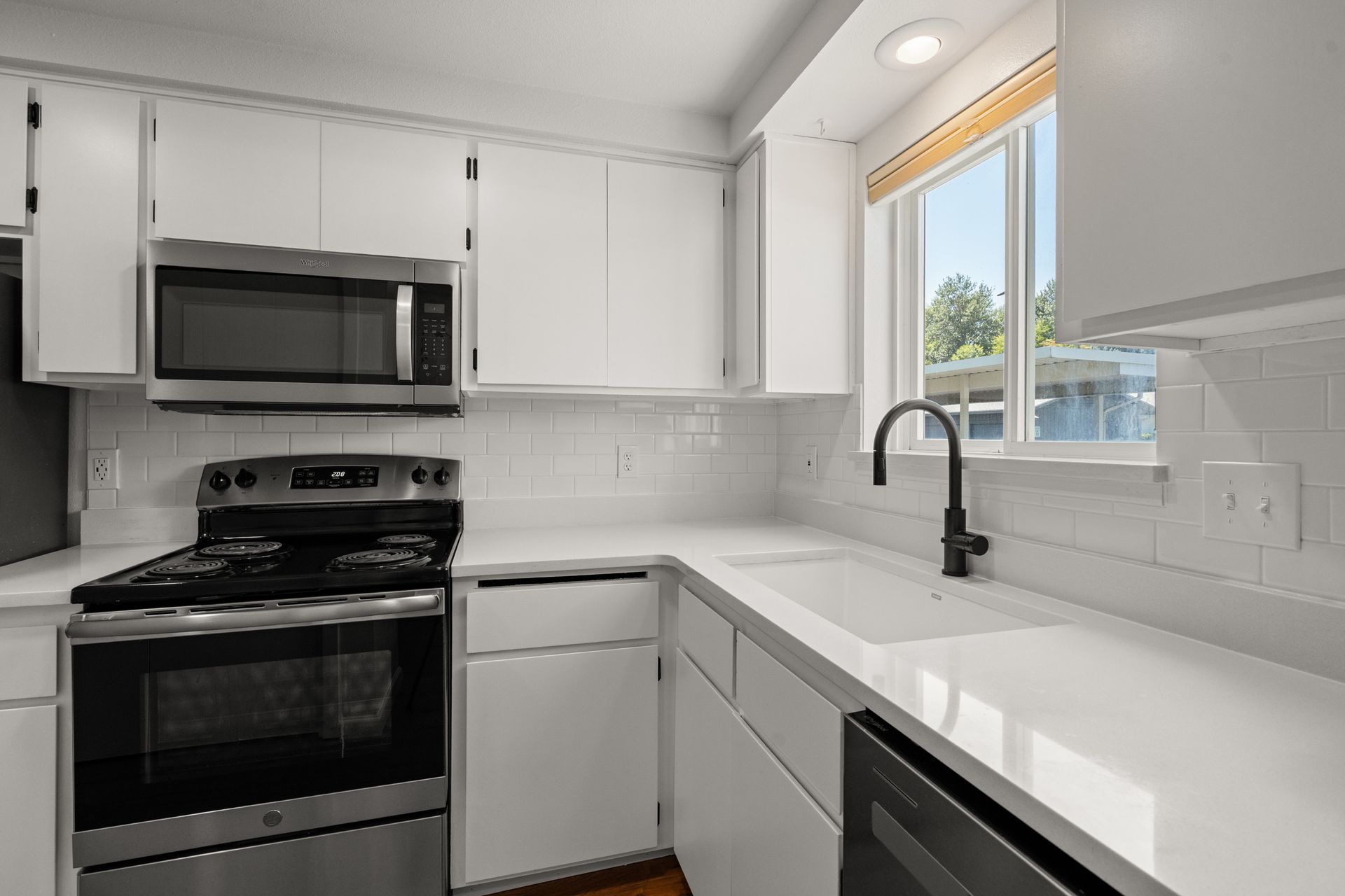 A kitchen with white cabinets , stainless steel appliances , a sink , and a window.