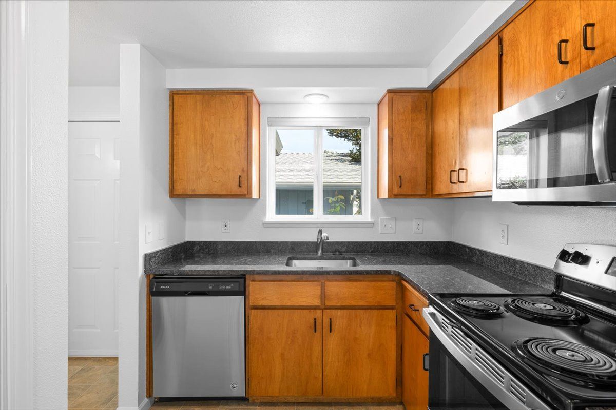A kitchen with wooden cabinets , stainless steel appliances , a sink , and a window.