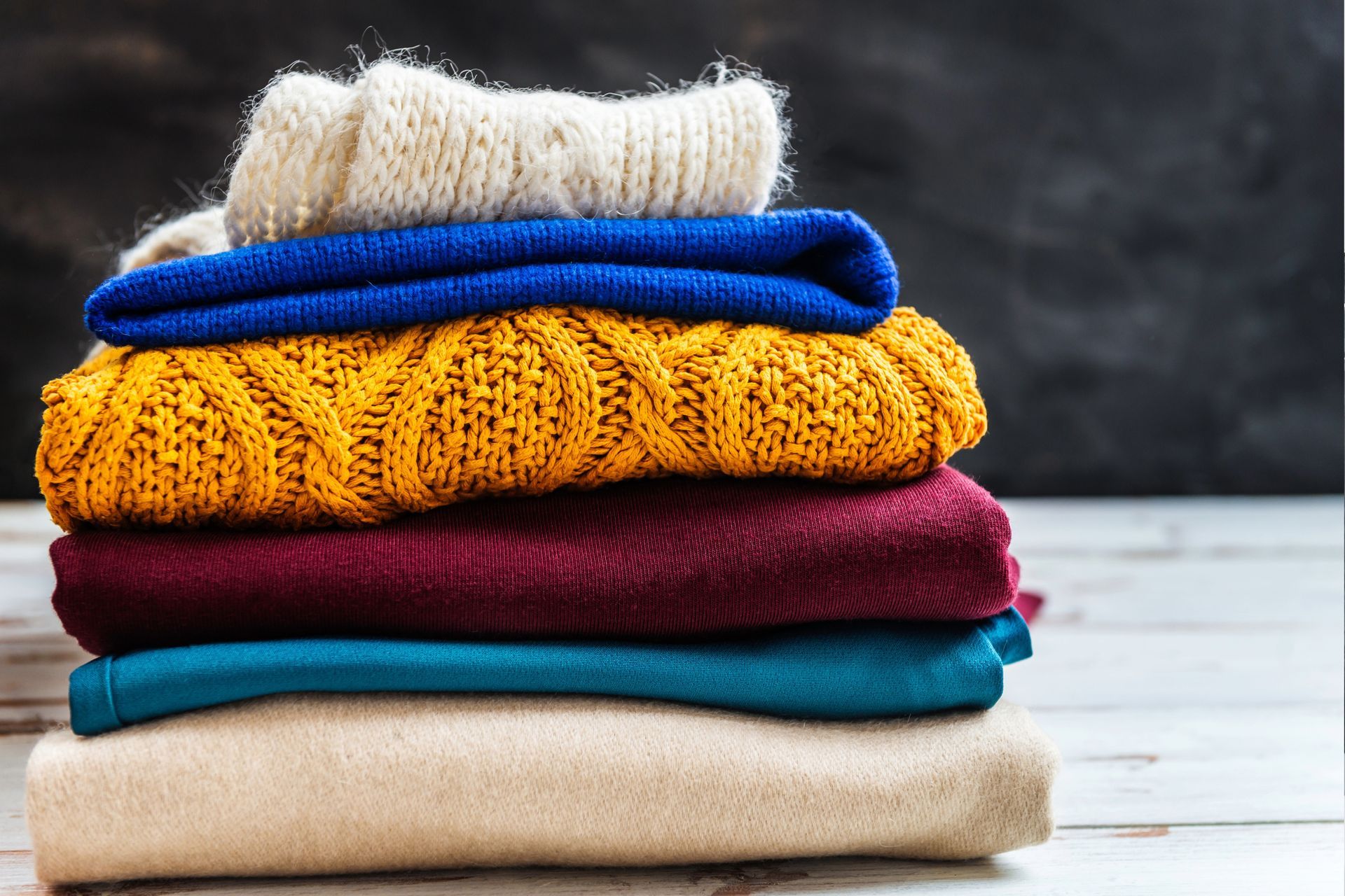 Stack of folded sweaters in various colors, including yellow, blue, and cream.