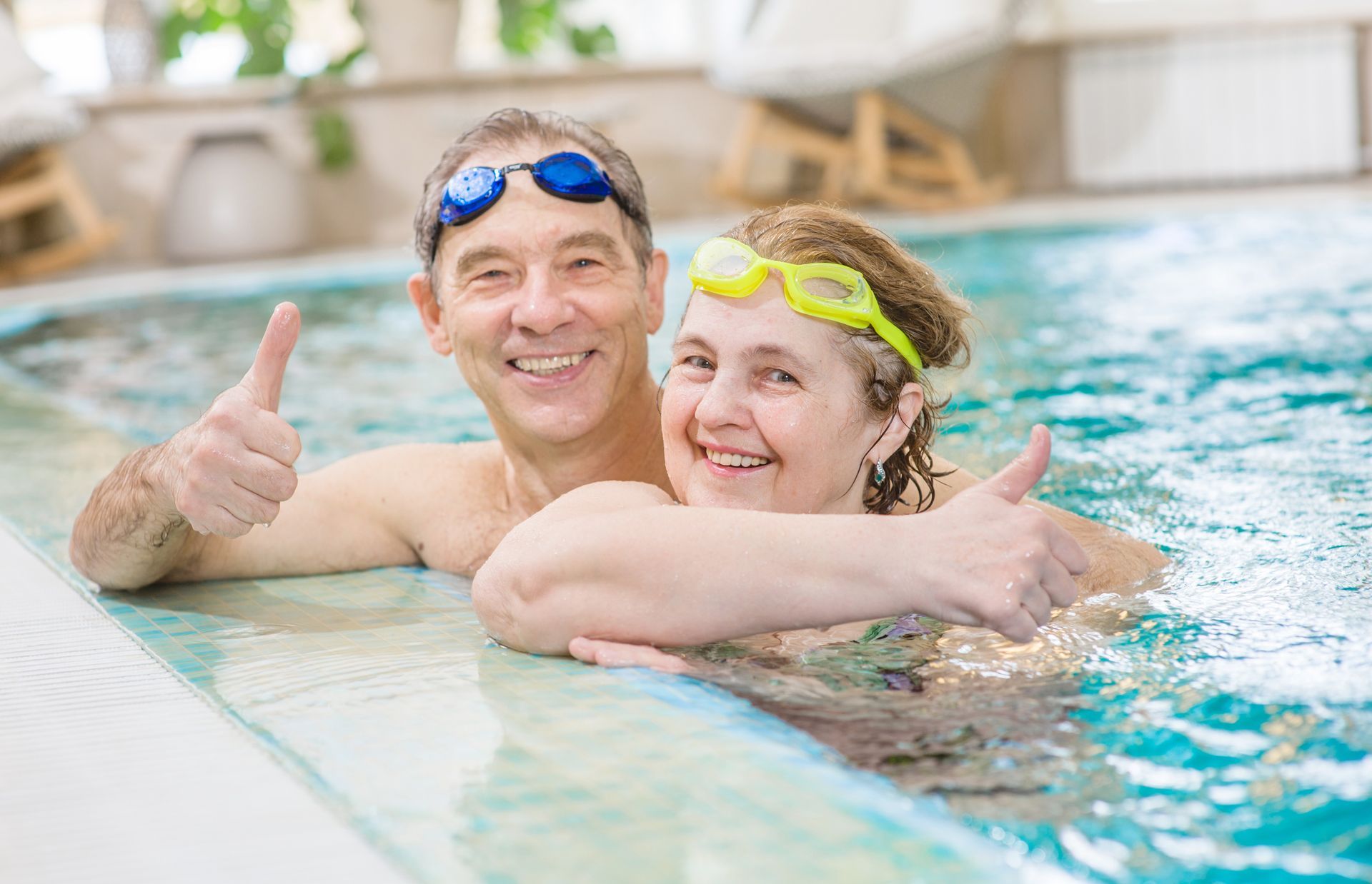 A man and a woman are giving a thumbs up in a swimming pool.