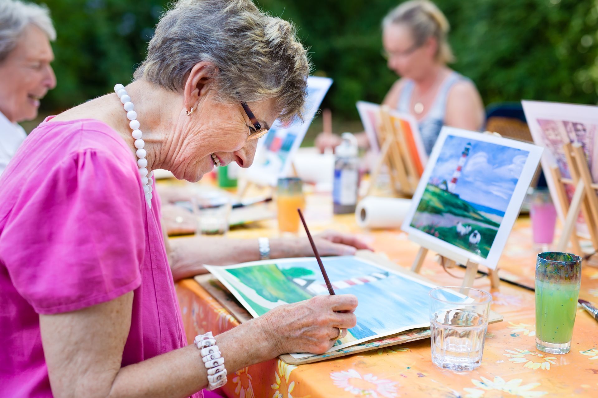 An elderly woman is sitting at a table painting a picture.