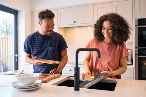Couple washing dishes in a modern kitchen. Man cleans cutting board, woman scrubs a dish at the sink.