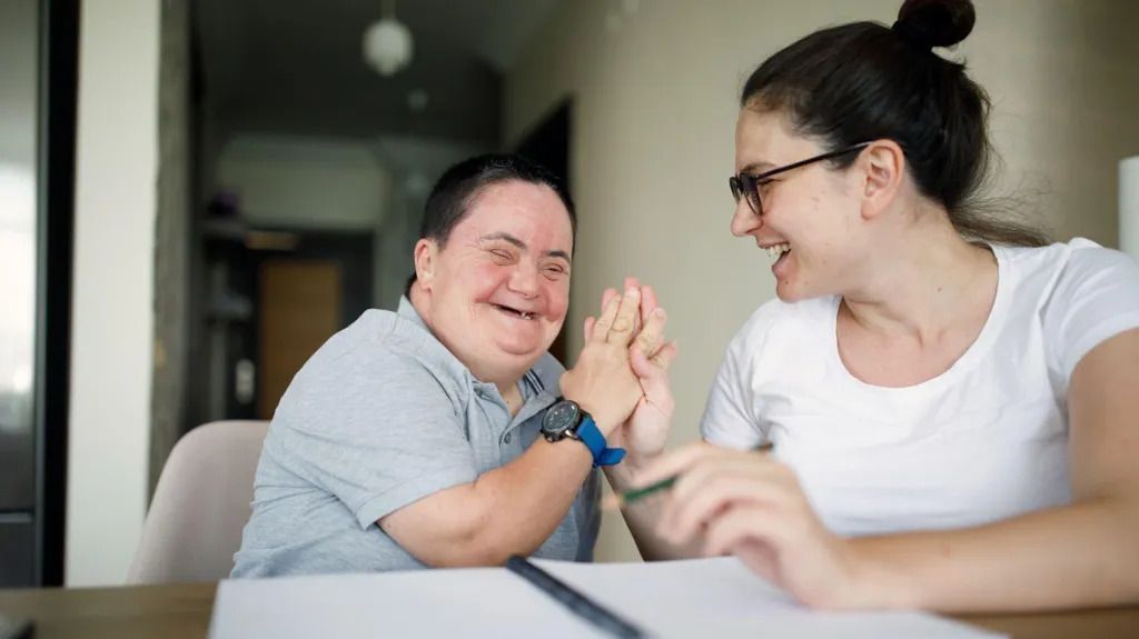 Man and woman high-fiving at a table, both smiling; indoor setting.