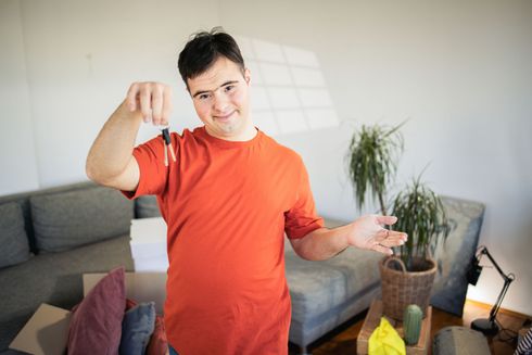 Man with Down syndrome holding keys, smiling, in a living room, ready to move in.