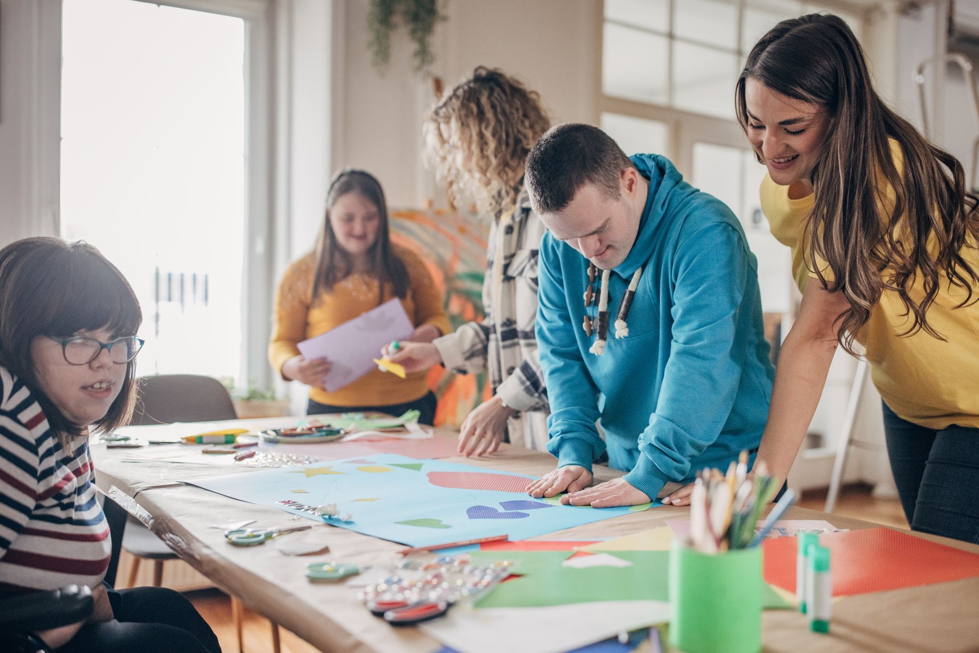 People crafting together at a table. Arts & crafts setting with colorful paper, scissors, and pencils.