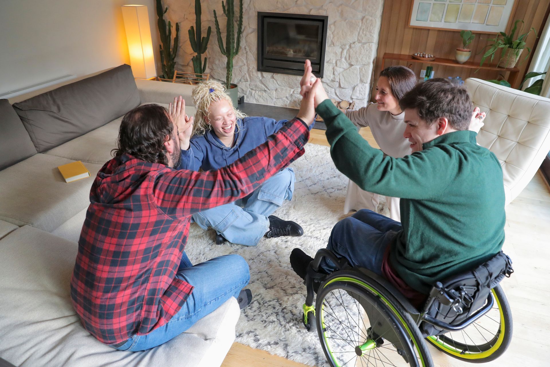 Four people high-fiving in a living room; one uses a wheelchair.
