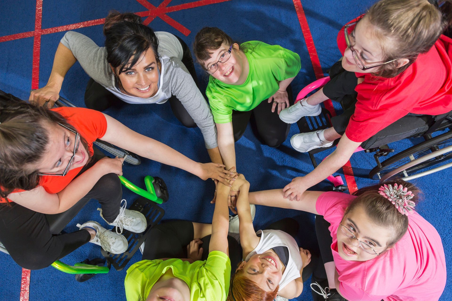 Group of people with disabilities joining hands, smiling, in a gym.